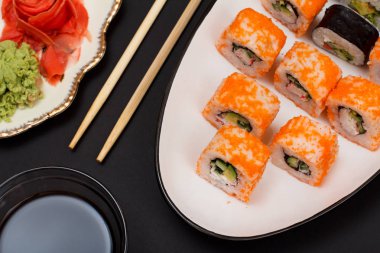 Suşi nori, pirinç, avokado, salatalık, seramik plaka üzerinde uçan balık karaca parçaları ile alır. Kırmızı Turşu Zencefil ve wasabi ile plaka. Soya sosu ve ahşap sopa ile top. Siyah arka plan.