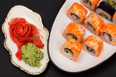 Uramaki California. Suşi rulo nori, pirinç, adet avokado, salatalık, seramik plaka üzerinde uçan balık karaca ile dekore edilmiştir. Kırmızı Turşu Zencefil ve wasabi ile plaka. Üstten görünüm. Siyah arka plan.