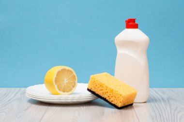 Bulaşık yıkama sıvı, temiz tabak, limon ve mavi zemin üzerine sünger plastik şişe. Yıkama ve Temizleme kavramı.