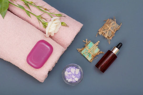 Spa products for massage, facial and body care. Natural sea salt, homemade soap, bottle of aromatic oil and pink towels with flower on gray background. Spa and bodycare concept. Top view.