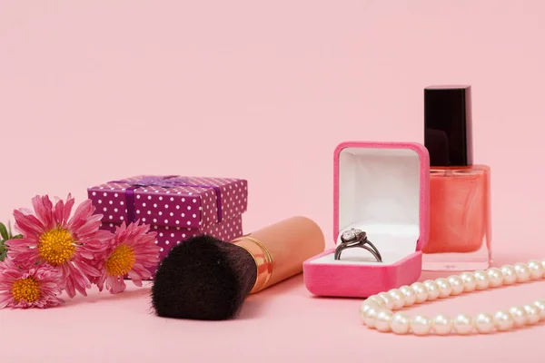Ring in a box, nail polish, brush, beads, gift box and flowers on a pink background. Women jewelry, cosmetics and accessories.