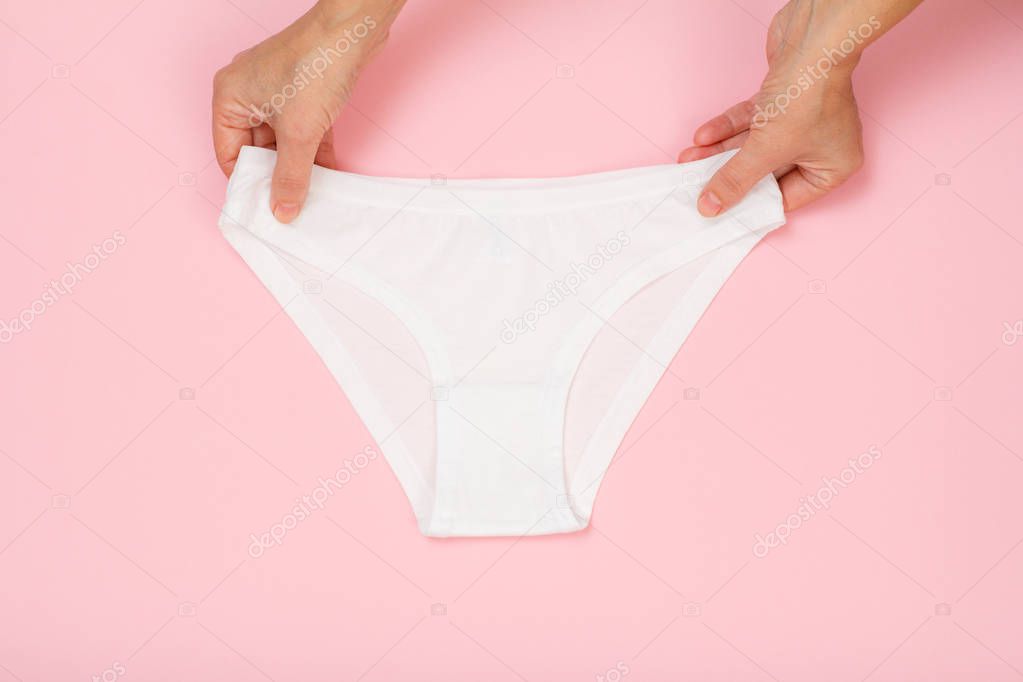 Women's hands holding beautiful cotton brown panties on pink background. Woman underwear set. Top view.