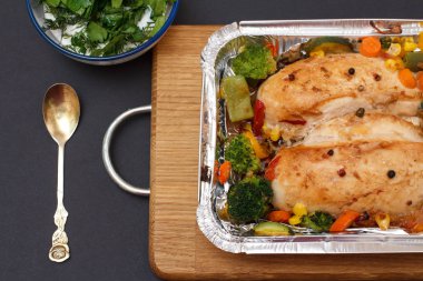 Fırında tavuk göğsü veya fileto sebze ve yeşillik bir ahşap kesme tahtası üzerinde metal kap içinde. Sos ve kaşık ile cam kase. Üstten görünüm.