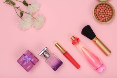 Hediye kutusu, şişe parfüm, ruj, fırça ve pembe bir arka plan üzerinde çiçekler. Kadın kozmetik ve aksesuarları. Üstten görünüm.