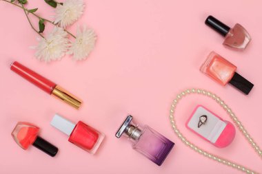 Yüzük ile boncuklar, şişe tırnak cilası ve parfüm, ruj ve çiçek pembe bir arka plan üzerinde kutu. Kadın kozmetik ve aksesuarları. Üstten görünüm.
