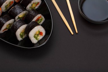 Suşi nori deniz yosunu yaprak avokado ve kırmızı balık ile seramik plaka üzerinde rulo. Soya sosu ve ahşap sopa ile top. Siyah arka plan ile üstten görünüm.
