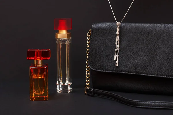 Bottles with women perfume, handbag and necklace in a black background. Women products.