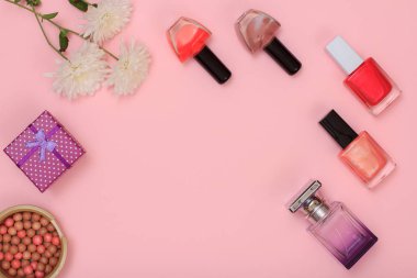 Hediye kutusu, toz, şişe parfüm ve tırnak cilası ve pembe bir arka plan üzerinde çiçekler. Kadın kozmetik ve aksesuarları. Üstten görünüm.