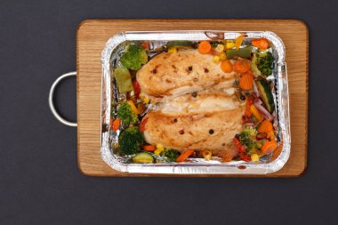 Fırında tavuk göğsü veya fileto sebze ve yeşillik bir ahşap kesme tahtası üzerinde metal kap içinde. Üstten görünüm.
