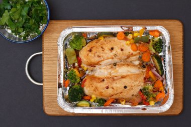 Fırında tavuk göğsü veya fileto sebze ve yeşillik bir ahşap kesme tahtası üzerinde metal kap içinde. Bir köşede soslu cam kase... Üstten görünüm.