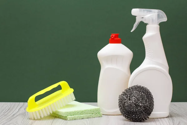 Plastic bottles of dishwashing liquid, glass and tile cleaner, brush, sponges on green background. Washing and cleaning concept.