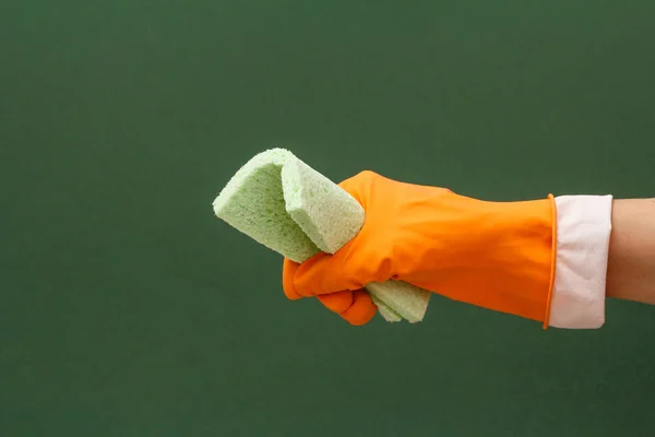 Woman\'s hand in orange protective glove with sponge on green background. Washing and cleaning concept.