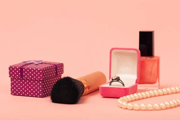 Gift box, brush, ring in a box, nail polish and beads on a pink background. Women jewelry, cosmetics and accessories.