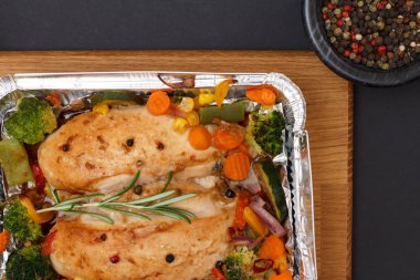 Fırında tavuk göğsü veya fileto sebze ve yeşillik bir ahşap kesme tahtası üzerinde metal kap içinde. Yenibahar biber ile cam kase. Üstten görünüm.