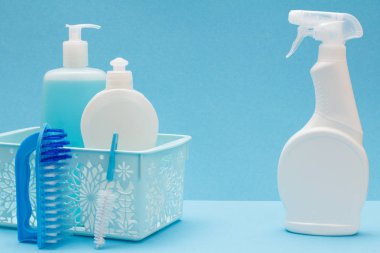 Bulaşık yıkama sıvı, cam ve döşeme temizleyici içinde sepeti ve fırçalar mavi zemin üzerine plastik şişe. Yıkama ve Temizleme kavramı.