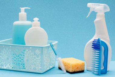 Plastik şişe bulaşık sıvı, cam ve döşeme temizleyici içinde sepeti, sünger ve fırçalar mavi zemin üzerine. Yıkama ve Temizleme kavramı.