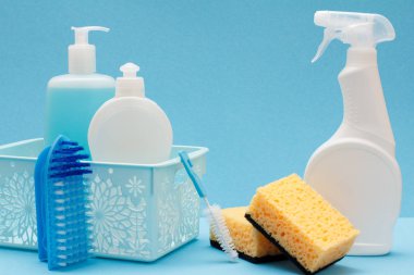 Bulaşık yıkama sıvı, cam ve döşeme temizleyici içinde sepeti, sünger ve fırçalar mavi zemin üzerine plastik şişe. Yıkama ve Temizleme kavramı.