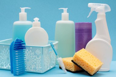 Bulaşık deterjanı, cam ve döşeme temizleyici sepeti, süngerler, çöp torbaları ve fırçalar mavi zemin üzerine plastik şişe. Yıkama ve Temizleme kavramı.