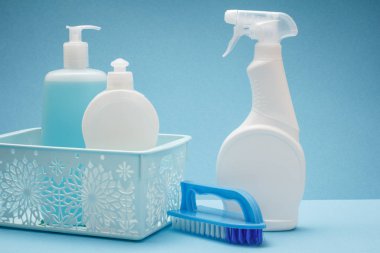 Bulaşık yıkama sıvı, cam ve döşeme temizleyici içinde sepeti ve mavi zemin üzerine fırça plastik şişe. Yıkama ve Temizleme kavramı.