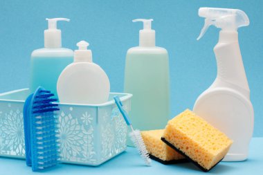 Bulaşık yıkama sıvı, cam ve döşeme temizleyici içinde sepeti, sünger ve fırçalar mavi zemin üzerine plastik şişe. Yıkama ve Temizleme kavramı.