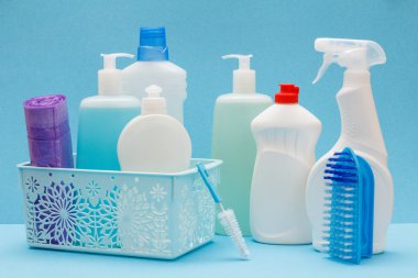 Bulaşık deterjanı, cam ve döşeme temizleyici sepeti, süngerler, çöp torbaları ve fırçalar mavi zemin üzerine plastik şişe. Yıkama ve Temizleme kavramı.