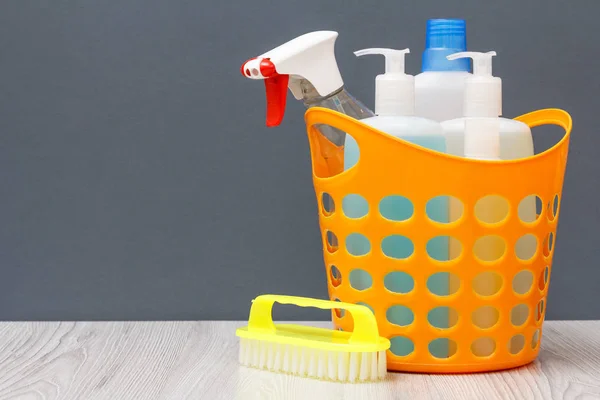Plastic basket with bottles of dishwashing liquid, glass and tile cleaner, detergent for microwave ovens and stoves with brush on gray background. Washing and cleaning concept.