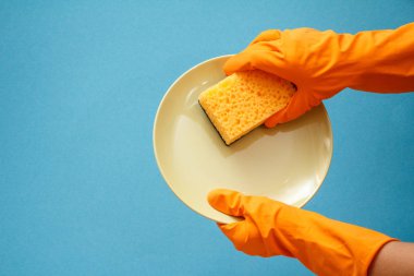 Kadınların elleri plaka ve mavi zemin üzerine sünger ile turuncu koruyucu eldiven. Yıkama ve Temizleme kavramı.
