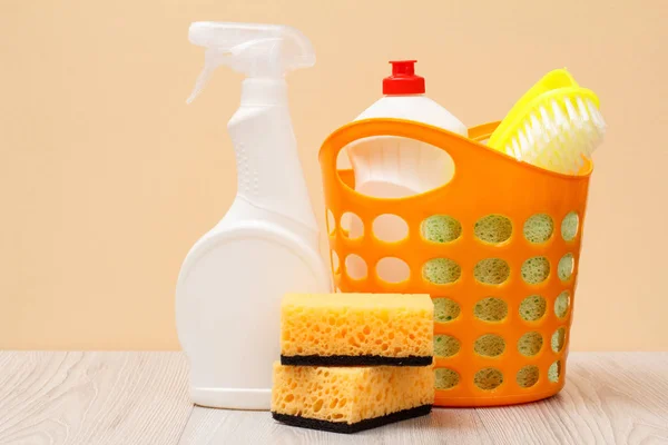 Plastic bottles of dishwashing liquid, glass and tile cleaner, detergent for microwave ovens and stoves, basket, brush, sponges on beige background. Washing and cleaning concept.