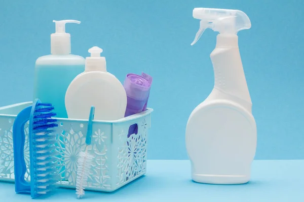 Plastic bottles of dishwashing liquid, glass and tile cleaner, garbage bags in basket, brushes and detergent for microwave ovens and stoves on blue background. Washing and cleaning concept.