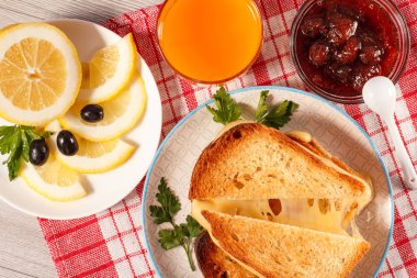 Dilim ekmek peynir ve yeşil maydanoz beyaz tabakta, cam og portakal suyu, limon, zeytin, kaşık ve cam kase kırmızı mutfak peçete ile çilek reçeli ile tost. Kahvaltıda iyi yemek