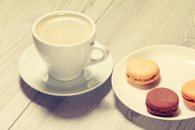 Kahve fincan tabağı ve lezzetli macarons kek gri ahşap arka plan beyaz porselen tabakta farklı renk.