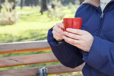 Kırmızı fincan kahve ile termos şehir parkta bankta oturan, holding kadının eller.