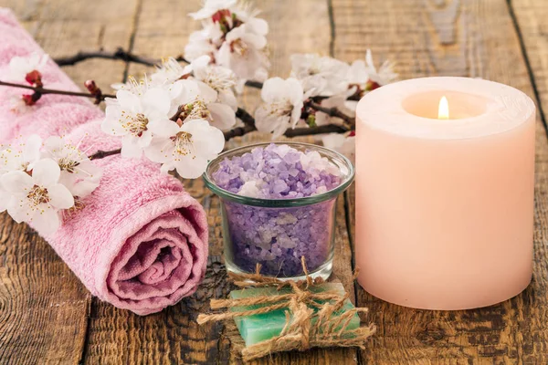 Handmade soap, sea salt in glass bowl with towel for bathroom procedures and burning candle with flowering branch of apricot tree. Spa products and accessories.