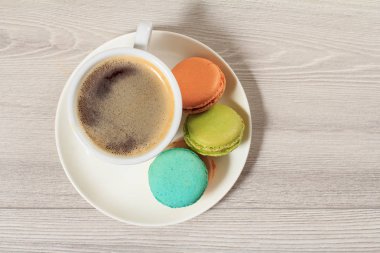 Fincan kahve ve lezzetli macarons kek farklı renk gri ahşap arka plan beyaz porselen tabakta. Üstten görünüm.