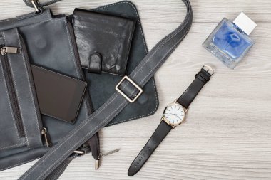 Cep telefonu ve cüzdanı, kol saati ve erkekler kolonya gri ahşap arka plan üzerinde olan erkekler için deri omuz çantası. Erkek aksesuarlar. Üstten Görünüm.