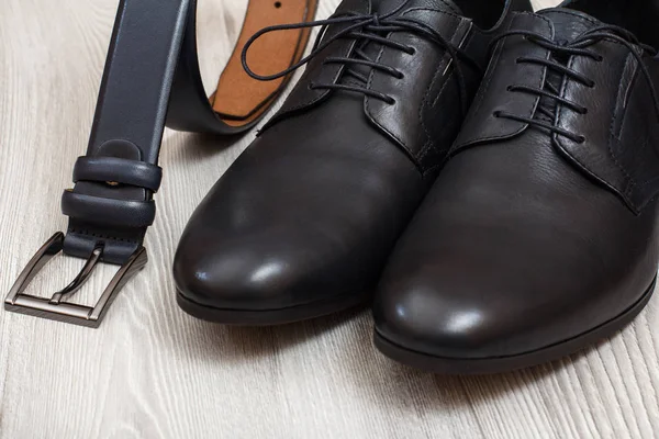 Pair of black leather men's shoes and leather belt for men on gray wooden boards. Men's accessories.
