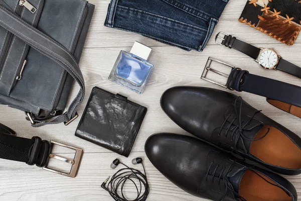 Shoulder bag, pair of black leather men\'s shoes, belts for men, jeans, men\'s cologne, wristwatch and purse on gray wooden boards. Men\'s accessories