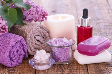Aromatik yağ, mum, deniz tuzu, sabun, Lila çiçek ve havlu banyo yordamlar ahşap kurullarında için kase yanan kırmızı şişe. Spa ürünleri ve aksesuarları.