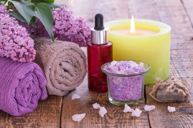 Leylak çiçekleri, havlular, aromatik yağ ile kırmızı şişe, yanan mum, deniz tuzu ve sabun ile kase.