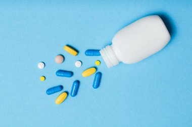 White bottle with different pills and capsules on blue background