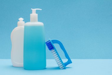 Mavi arka planda bulaşık sıvısı ve fırça şişeleri.