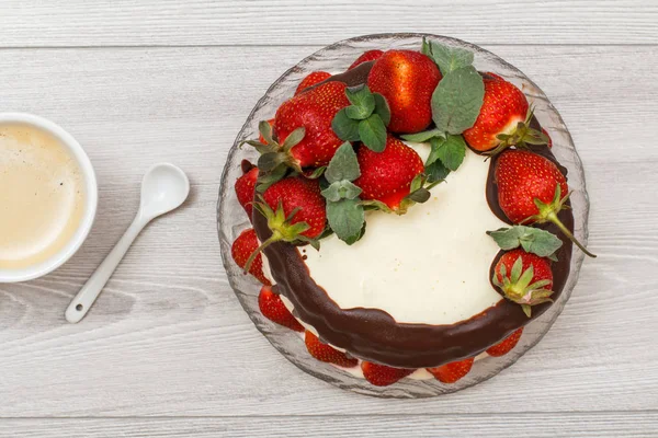 Домашній шоколадний торт, прикрашений свіжою полуницею на скляній тарілці та чашкою кави на сірому фоні . — стокове фото
