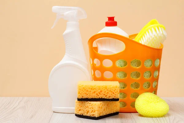 Bottles of dishwashing liquid, basket, brush and sponges on beige background. — Stock Photo, Image