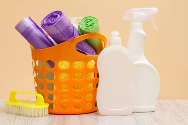 Bottles of dishwashing liquid, basket with garbage bags and brush on wooden desk. — Stock Photo, Image