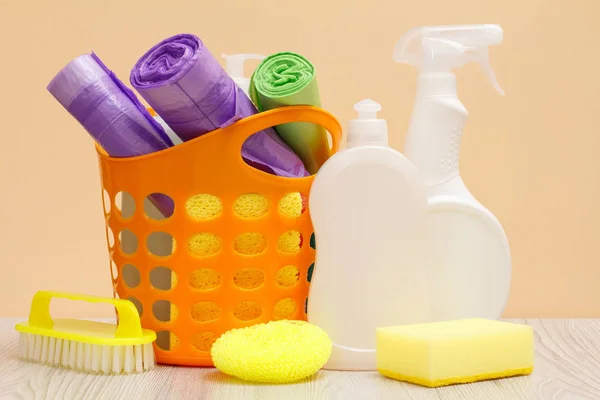Bottles of dishwashing liquid, basket with garbage bags and sponges, brush on wooden desk. — Stock Photo, Image