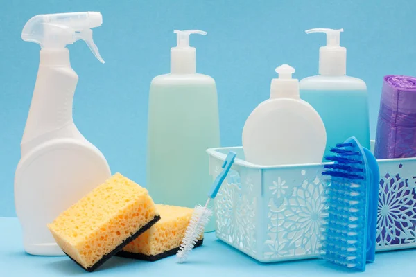 Botellas de líquido lavavajillas en cesta, esponjas y cepillos sobre fondo azul . — Foto de Stock