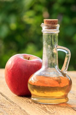 Cam şişede elma sirkesi ve yeşil doğal arka plan ile ahşap tahtalar üzerinde taze kırmızı elma.