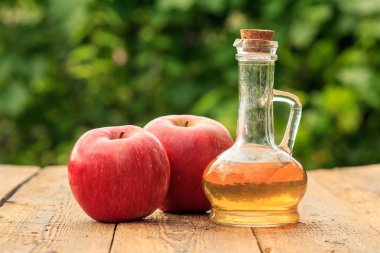 Cam şişede elma sirkesi ve yeşil doğal arka plan ile ahşap tahtalar üzerinde kırmızı elma.