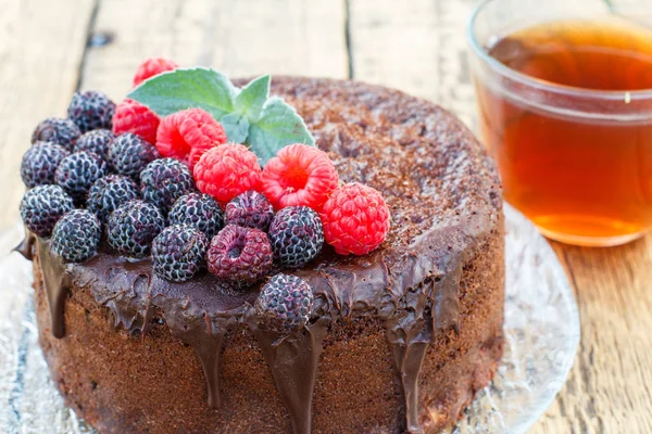 Pastel de chocolate casero decorado con frambuesas negras y rojas en plato de vidrio con taza de té . — Foto de Stock