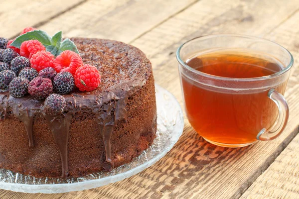 Pastel de chocolate casero decorado con frambuesas negras y rojas en plato de vidrio con taza de té . — Foto de Stock